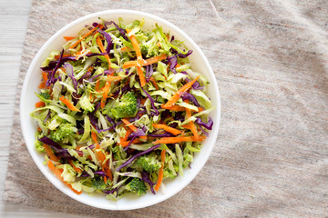 Homemade Raw Shredded Broccoli Slaw in a white bowl on cloth, overhead view. Top view, from above, flat lay. Copy space.