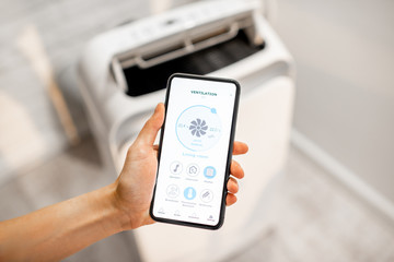 Woman holding smart phone with launched application for air condition control with ventilation unit...