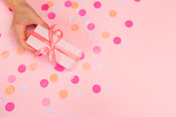 Woman presenting gift box top view on pastel pink background with pink confetti. Giving presents concept, card for Mother's Day, Women's Day or any other holiday or celebration - Image