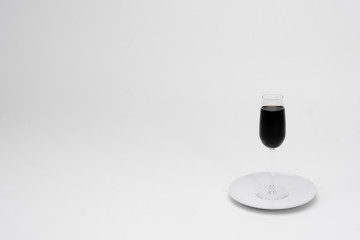 Empty glass with black liquid on a white background. Glass on a white plate. Minimalism. Isolated