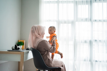 mother holding her son on lap when playing while sitting on the chair in the bedroom