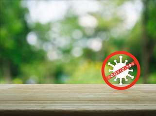 Stop COVID-19 outbreak icon on wooden table over blur green tree in park, Concept of novel...