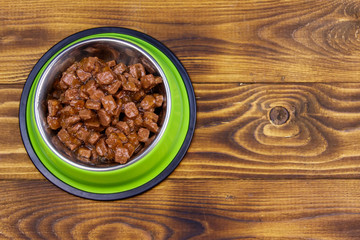 Canned food for cats or dogs in green metal bowl on wooden floor. Top view