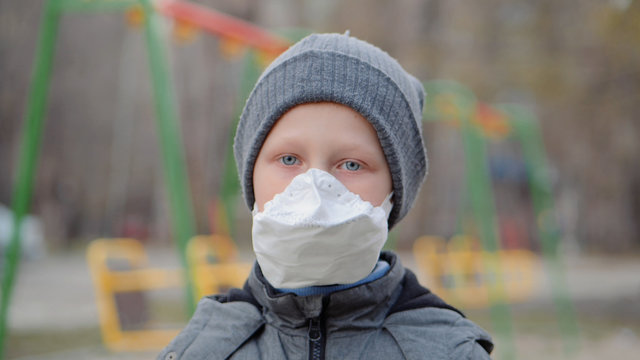 The boy adjusts his protective mask. In the background, Playground, closed to quarantine because of pandemic covid-19