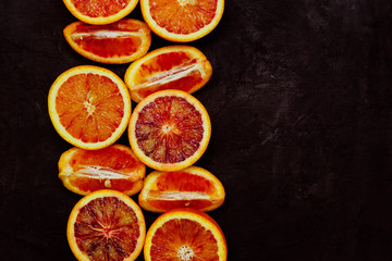 Top view of fresh blood orange halves and quaters on black background with copy space. Toned image.