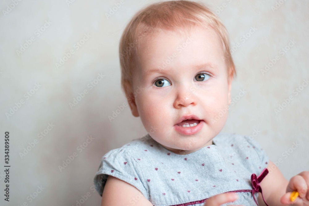 Wall mural little cute girl of caucasian appearance. cute baby with a blond moor. she is dressed in a gray dres