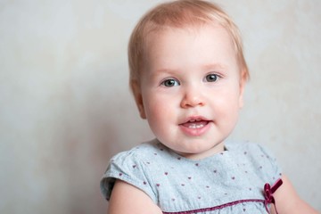 Naklejka premium Little cute girl of Caucasian appearance. Cute baby with a blond moor. She is dressed in a gray dress. In a home atmosphere. Home clothes. Child 1 year. Cheerful girl playing.