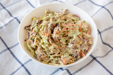 Homemade Creamy Broccoli Slaw in a white bowl on cloth, side view. Close-up.