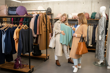 Young woman showing light blue cotton sweater to her friend during sale