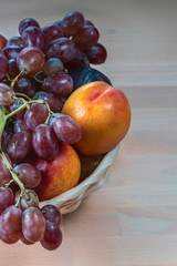 Naklejka na ściany i meble red grape berries and fresh fruits in a straw basket on a light wooden background
