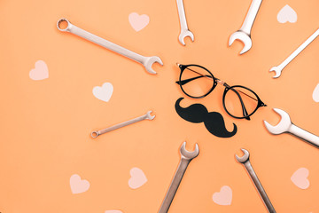 Holiday concept made with eyeglasses, stylish black paper photo booth props moustaches, many little hearts and combination wrenches on orange background. Copy space for inscriptions. Creative idea.