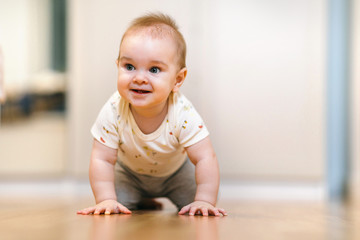 Naklejka premium A nine-month-old baby crawls on the floor, looks at the camera with an interest and delight