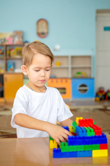 a boy plays at a table, folds plastic blocks and builds a garage for a toy car