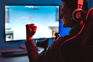 The smiling gamer with headphones playing video game on his personal computer - obrazy, fototapety, plakaty