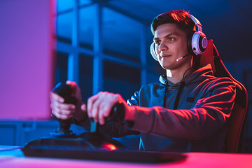 The gamer with headphones sitting and playing video games in the neon room