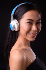 Face of happy young beautiful Asian woman listening to music