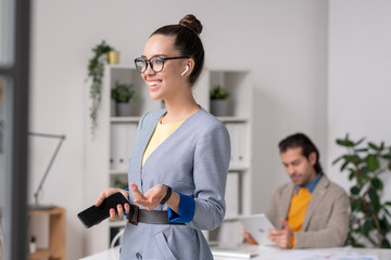 Cheerful female office worker with smartphone and earphones enjoying music
