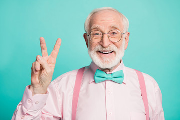 Hello. Closeup photo of amazing stylish clothes grandpa showing v-sign symbol greets friends wear specs pink shirt suspenders bow tie isolated bright teal color background