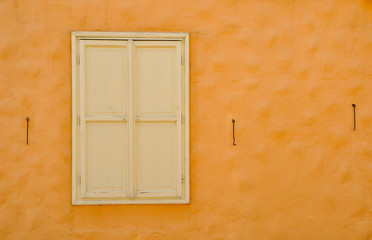 Vintage window on the orange old wall. Closed shutters with hooks. Abandoned building. Space for text.