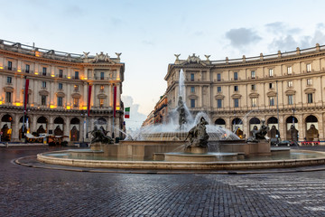 Republic Square in Rome, fountain and evening illumination of buildings, Italian flag in the background