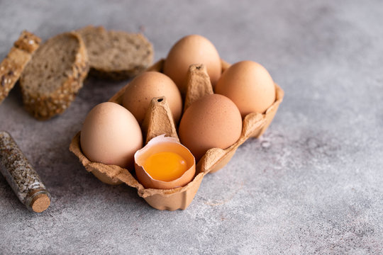 Raw chicken eggs and half broken among other eggs in box  for cooking on concrete background.Copy space