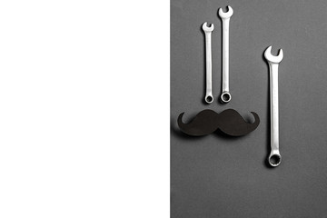 Father's Day Holiday Concept. Retro stylish black funny paper moustache and combination wrenches on grey and white background. Copy space for inscriptions.