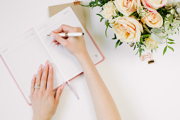 Woman hand write in notebook with bouquet and office supplies with copy space on white color paper...