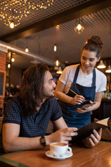 Happy young waitress in apron bending over one of clients of cafe