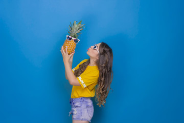 Happy girl holding a pineapple on a blue background
