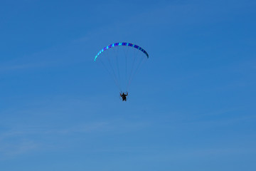 paraglider with a blue parachute flies against a cloudless sky