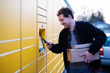 Mann mit Handy an einer Packstation will Pakete abgeben 