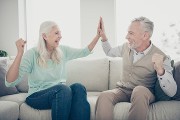 Portrait of lovely grandparents give high-five celebrate dressed teal brown pullover jeans trousers sit cozy divan scream shout in apartment indoors