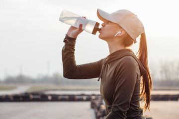 beautiful girl at morning workout drinks water from a bottle