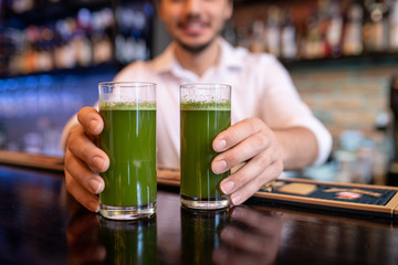 Hands of young waiter or barman holding two glasses of green vegetable cocktail