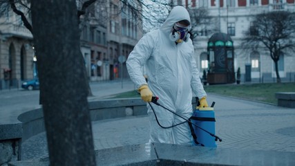 Close up view of specialist in protect wear pulverize disinfectant liquid on bench on empty street