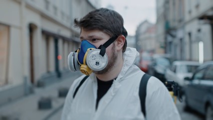 Fototapeta na wymiar Close up tilt-shift portrait of young european man in respirator face-protect in white wear look around in empty city alone