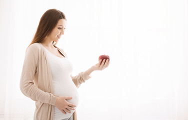 Pregnant woman eating apple in bed at home