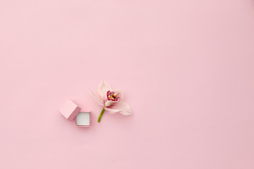 Pink box for an engagement ring and orchid flower on pink background, top view. Space for text