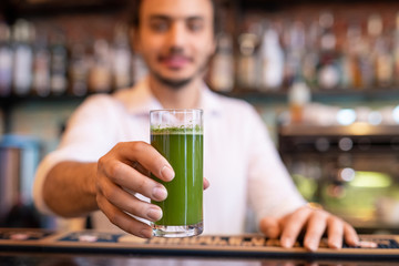 Hand of young barman holding glass of fresh vegetable smoothie over counter