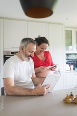 Happy pregnant woman with her husband sitting at home. Smiling couple consulting a book at the kitchen.