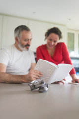 Happy pregnant woman with her husband sitting at home. Smiling couple consulting a book at the kitchen.