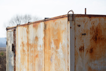 An iron old rusty garage stands in a field and pollutes nature.