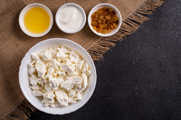 Cottage cheese in a white plate, separately honey, raisins on burlap, a dark background. Right space for text. Top view.