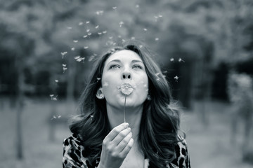 lost spring. Walk in the Park. Beautiful red-haired girl with freckles blowing on dandelion in park. Black and white photo.