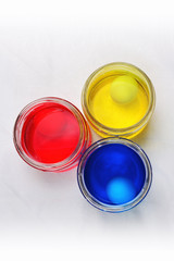 Three glass cans with blue yellow and red colorings for easter eggs proceeding on a linen tablecloth