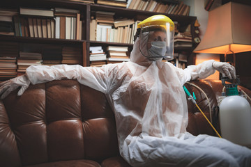 Person with protective antiviral mask, chemical decontamination sprayer bottle in home isolation.