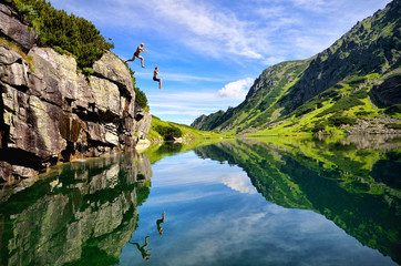 Young couple jump together into lake in mountains with beautiful blue water and reflexion.