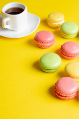 Breakfast Concept. Delicious colorful pastel macarons with coffee cup on yellow background.