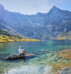 Man in white sitting on the rock in the middle of lake in beautiful clear summer mountains