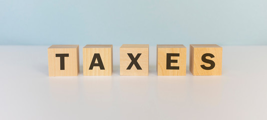 Word TAX. Wooden small cubes with letters isolated on blue background with copy space available.Business Concept image.